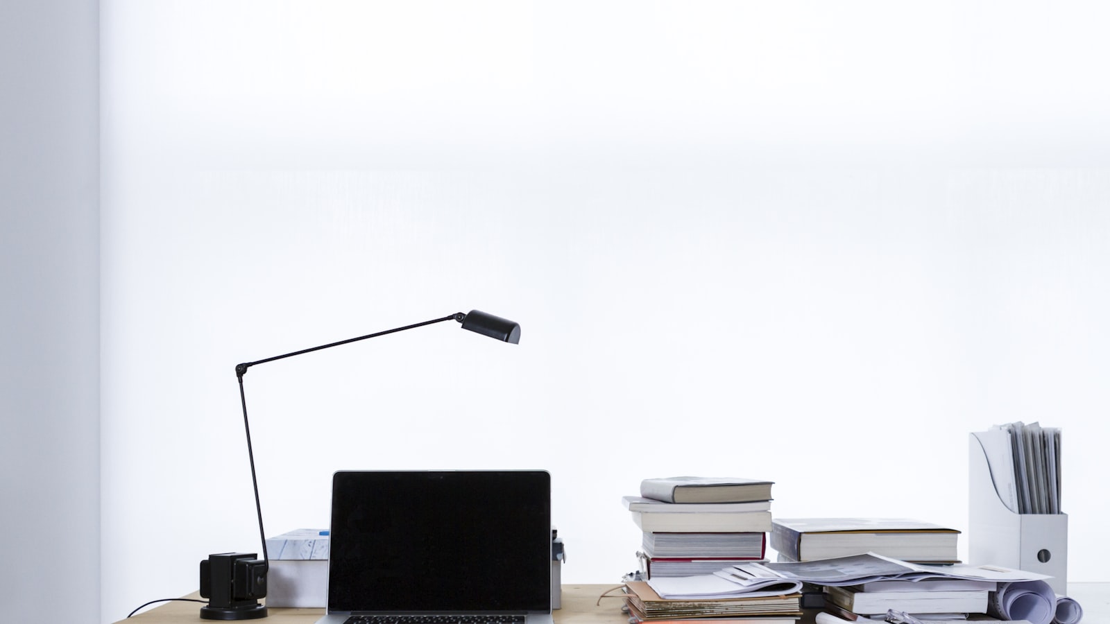 A minimalist desk with a laptop and stack of books, lit from a window